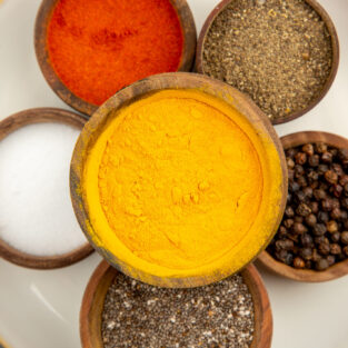 top-view-bowls-with-spices-round-plate-turmeric-salt-black-pepper-red-pepper-white-surface